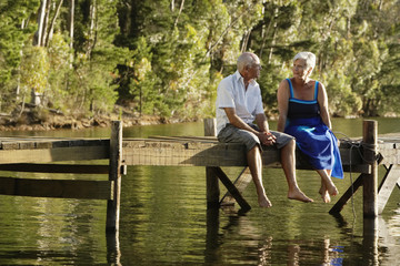 Full length of happy senior couple sitting on pier at lake