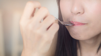 Young Asian woman, lady taste some food or beverage by hold spoon touch lips