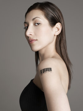 Portrait of a young woman with barcode tattoo on her arm against gray background