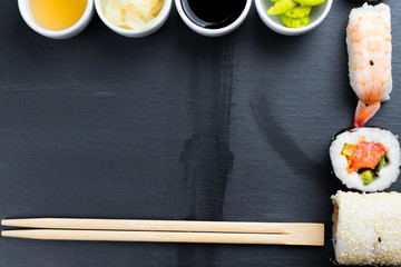 Japanese sushi with chopsticks on black kitchen slate plate.