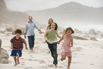 Happy children running on beach with parents walking in background