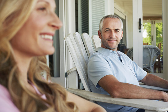 Portrait Of Middle Aged Man Sitting On Chair With Woman In Foreground At Porch