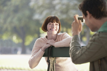 Cropped man photographing smiling young woman on bench