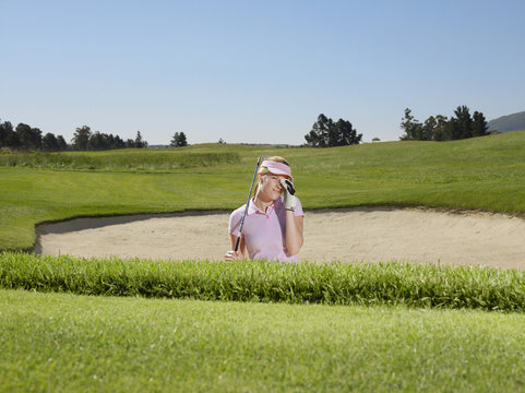 Young disappointed female golfer in sand trap