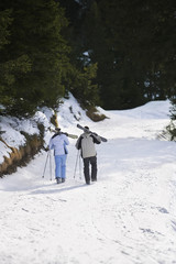 Full length rear view of a skiing couple carrying skis on shoulders on ski slope