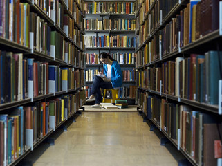 Female student reading by bookshelves in library 