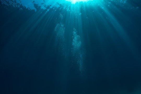 Air bubbles underwater in deep blue ocean with sunrays and water surface