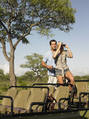 Young couple on safari standing in jeep and looking through binoculars © MDBPIXS