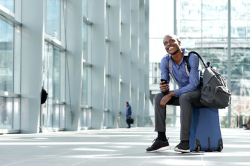 cheerful businessman sitting with luggage and cellphone at station