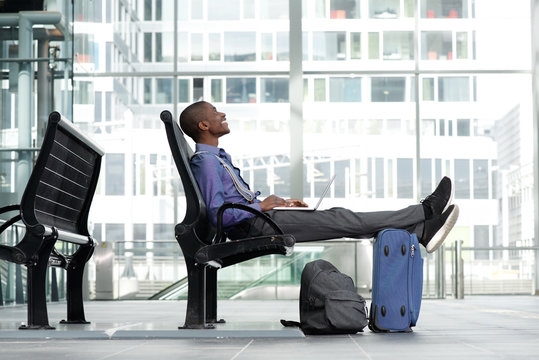 smiling young businessman sitting with laptop and luggage