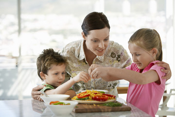 Happy mother helping children to prepare meal in kitchen