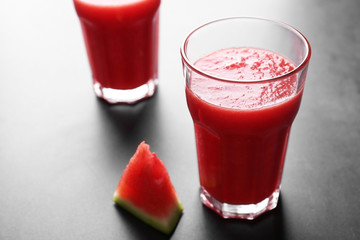 Glasses with smoothie and watermelon slice on grey table
