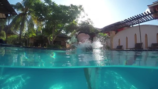 CLOSE UP: Peaceful young woman jumping into swimming pool head first and diving