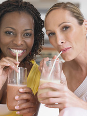 Portrait of two smiling multiethnic women drinking milkshake
