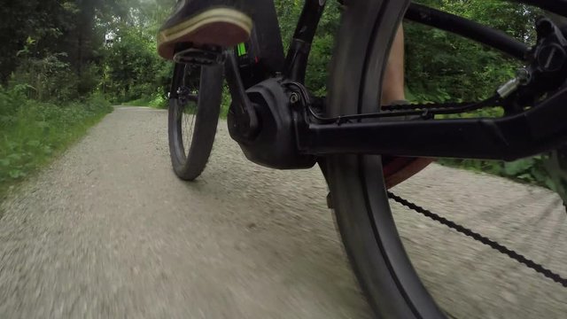 CLOSE UP: Biker riding electric bicycle on gravel dirt road through sunny forest