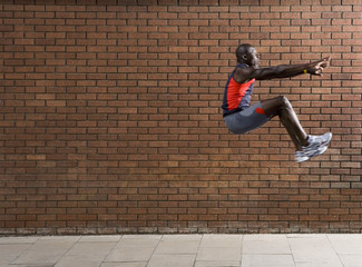 Side view of an African American man jumping against brick wall