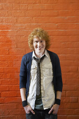 Portrait of happy young man with hands in pockets standing against brick wall