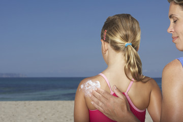 Closeup of a cropped woman applying sunscreen to girl on beach