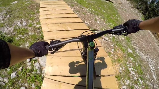FPV: Beginner biker riding downhill along the easy wooden trail in bike park