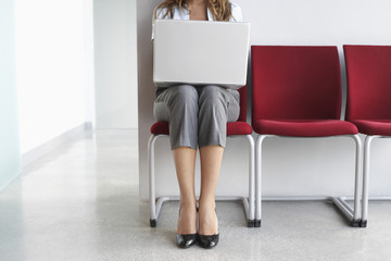 Lowsection of a female executive using laptop on chair in corridor