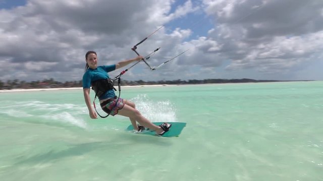 SLOW MOTION: Smiling surfer girl kitesurfing past the camera in blue lagoon