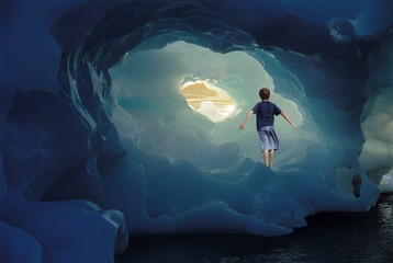Rear view of little boy with arms outstretched standing inside iceberg