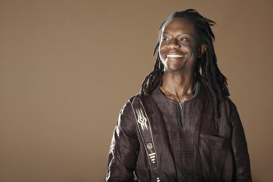 Smiling African American man with dreadlocks looking away on brown background