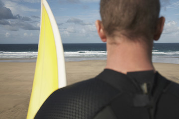 Rear view closeup of male surfer with surfboard on beach looking at sea