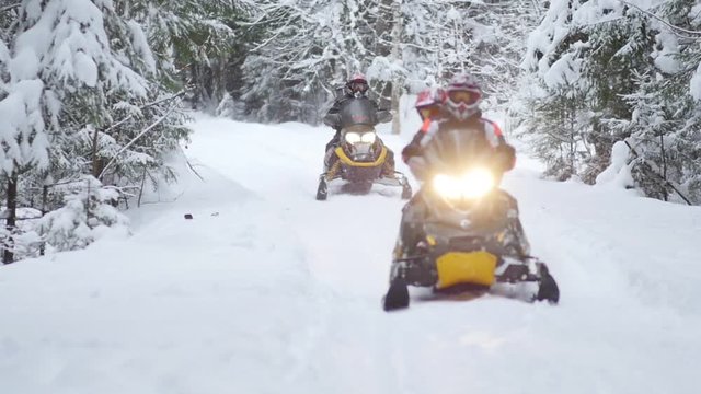 Slow motion of two snowmobiles on snowy road in the forest