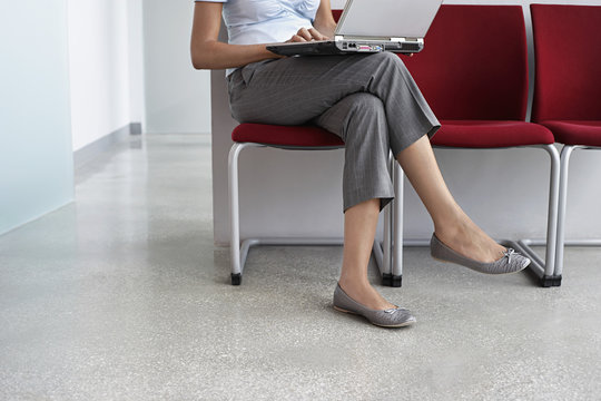 Lowsection of a female executive using laptop on chair in corridor