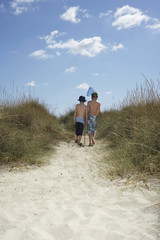 Full length rear view of two boys walking on sand dunes with fishing net