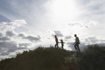 Silhouetted image of parents and daughter walking on sand dunes at beach