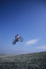 Low angle view of a man on mountain bike jumping against blue sky