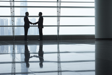 Fototapeta na wymiar Full length side view of businessmen shaking hands in airport terminal