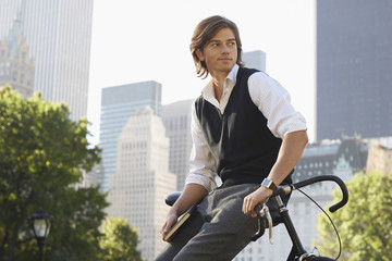 Fototapeta na wymiar Handsome young businessman leaning on bicycle in city park