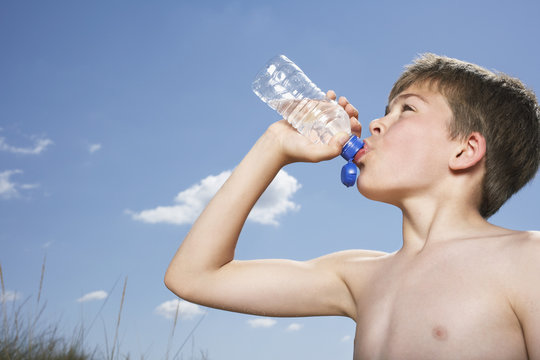 Side view of a shirtless boy drinking from water bottle against sky