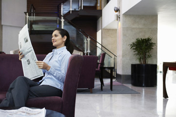 Happy young businesswoman reading newspaper in hotel lobby