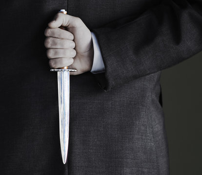 Closeup midsection of businessman holding knife against black background