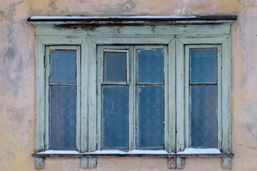 Fototapeta na wymiar Ветхие окна с деревянными рамами старого жилого дома с потрескавшейся штукатуркой 
