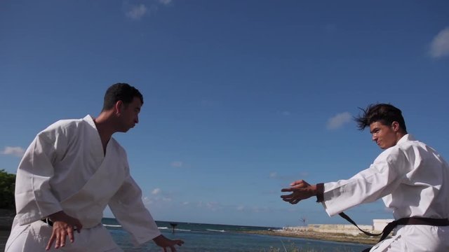Young people, athletes, sport activity, combat and extreme sports, hispanic men training in karate and traditional martial arts. Simulation of fight on the beach near the sea