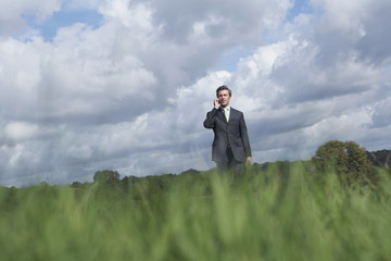 Businessman using mobile phone in meadow against cloudy sky