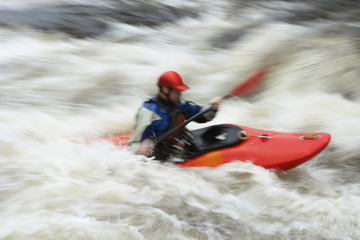 Side view of a blurred man kayaking in rough river