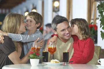 Happy young children embracing parents at restaurant table