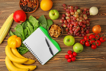 Notebook with fruits and vegetables on wooden background