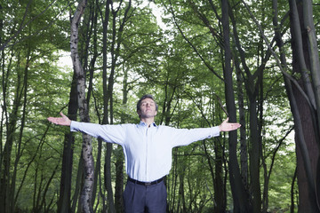 Businessman with arms outstretched standing in forest