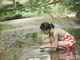 Side view of a young mixed race woman squatting in forest lake with hands cupped