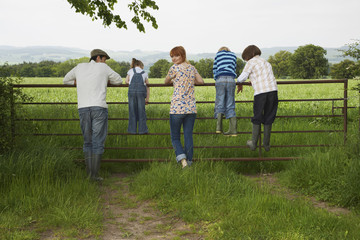 Obraz premium Full length rear view of couple with three children looking at lush landscape by fence