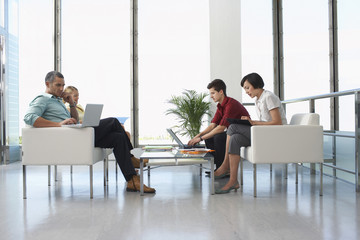 Full length side view of four business people sitting in modern waiting room at office