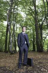 Full length portrait of confident businessman with hands in pockets standing in forest