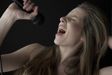 Closeup of passionate teenage girl singing into microphone on black background
